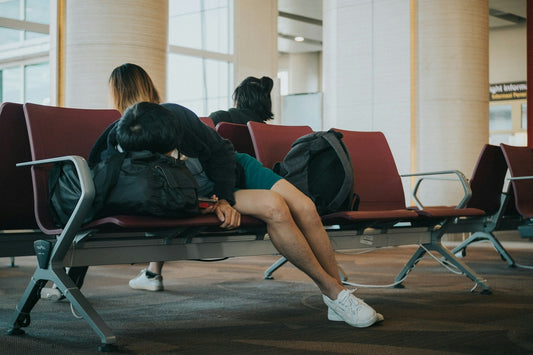 A man sleeping on a bench in an airport terminal surrounded by travel bags.