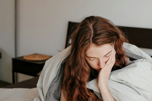 A frustrated woman with her head in her hand sitting on a bed.