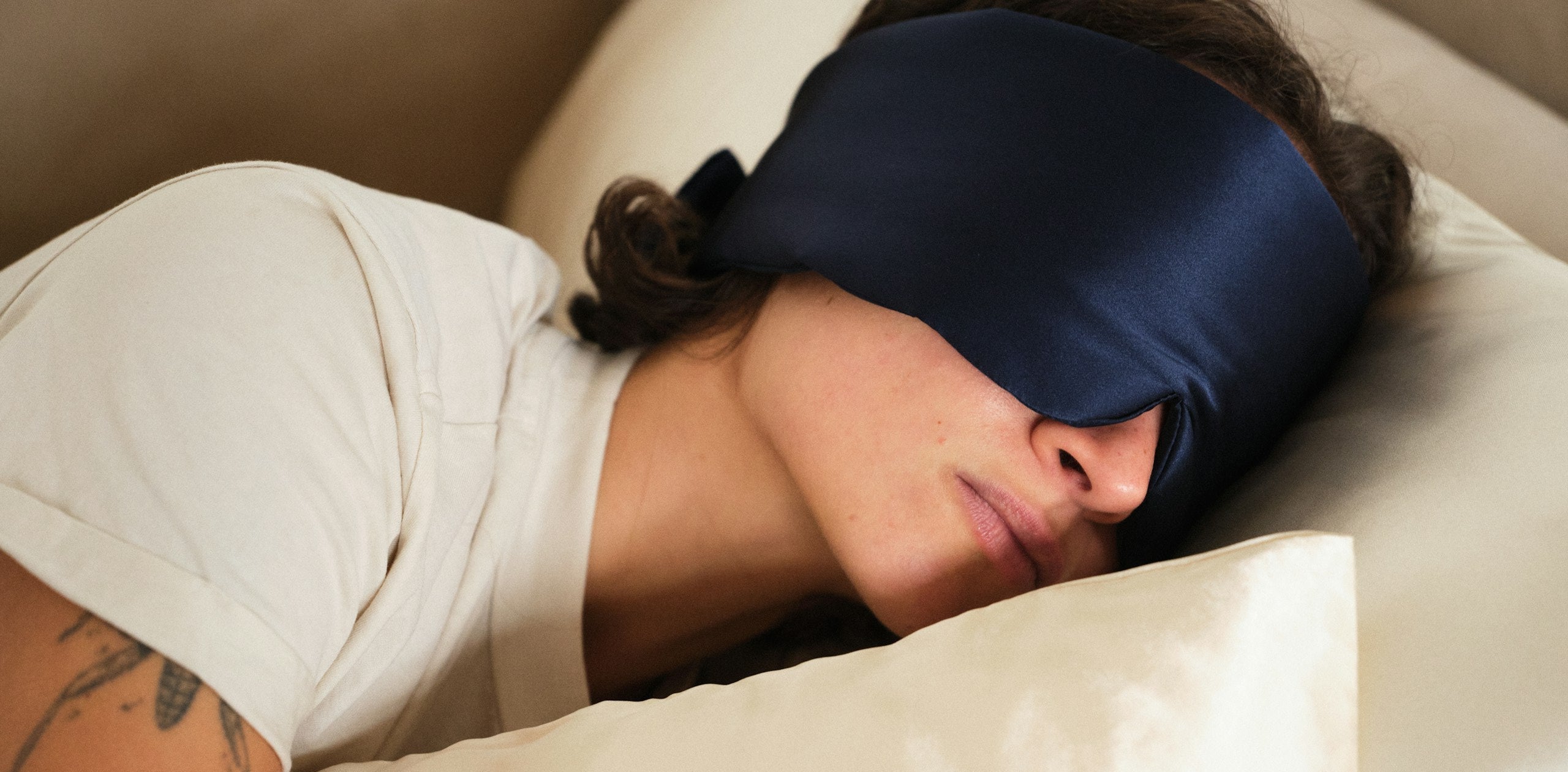 Person sleeping with a blue sleep mask on and a beige pillow.