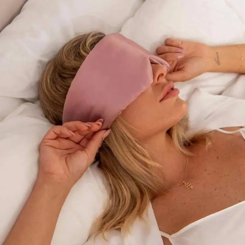 Person wearing a pink sleep mask on a white pillow