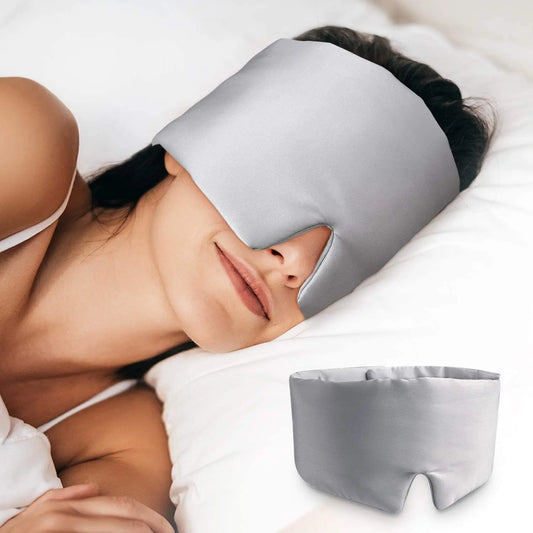 Person wearing a gray sleep mask with another identical mask on a white surface.