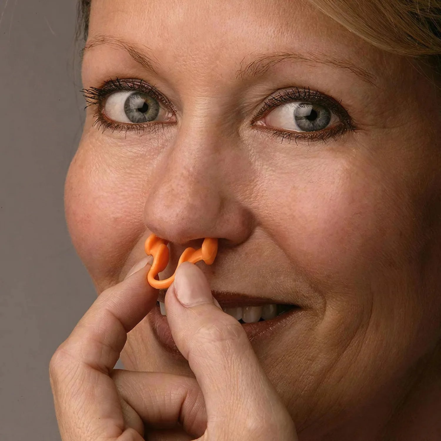 Woman using an orange nasal strip on a gray background