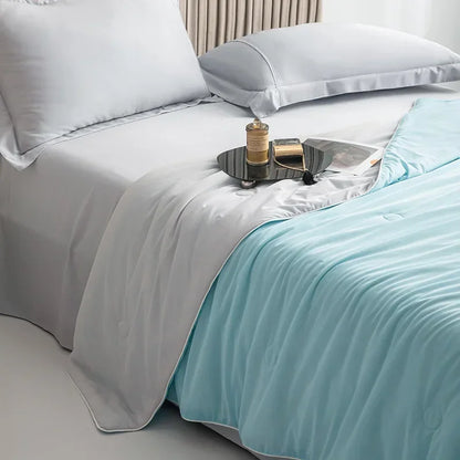 Bed with white bedding and a light blue throw blanket, featuring a small tray with items on a nightstand.