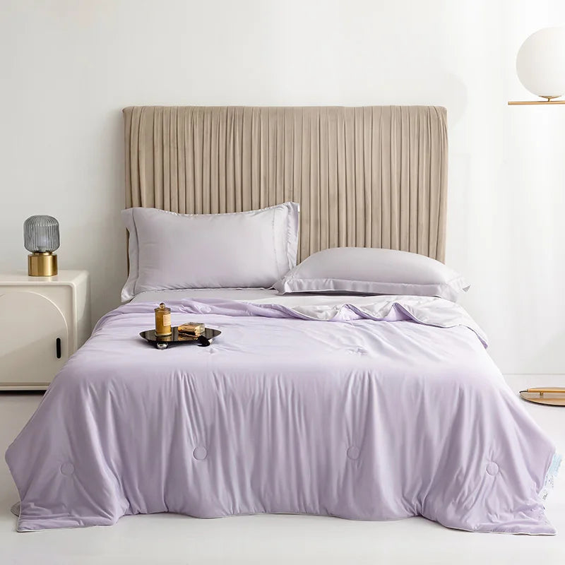 Bed with lavender bedding and white pillows in a bedroom setting.
