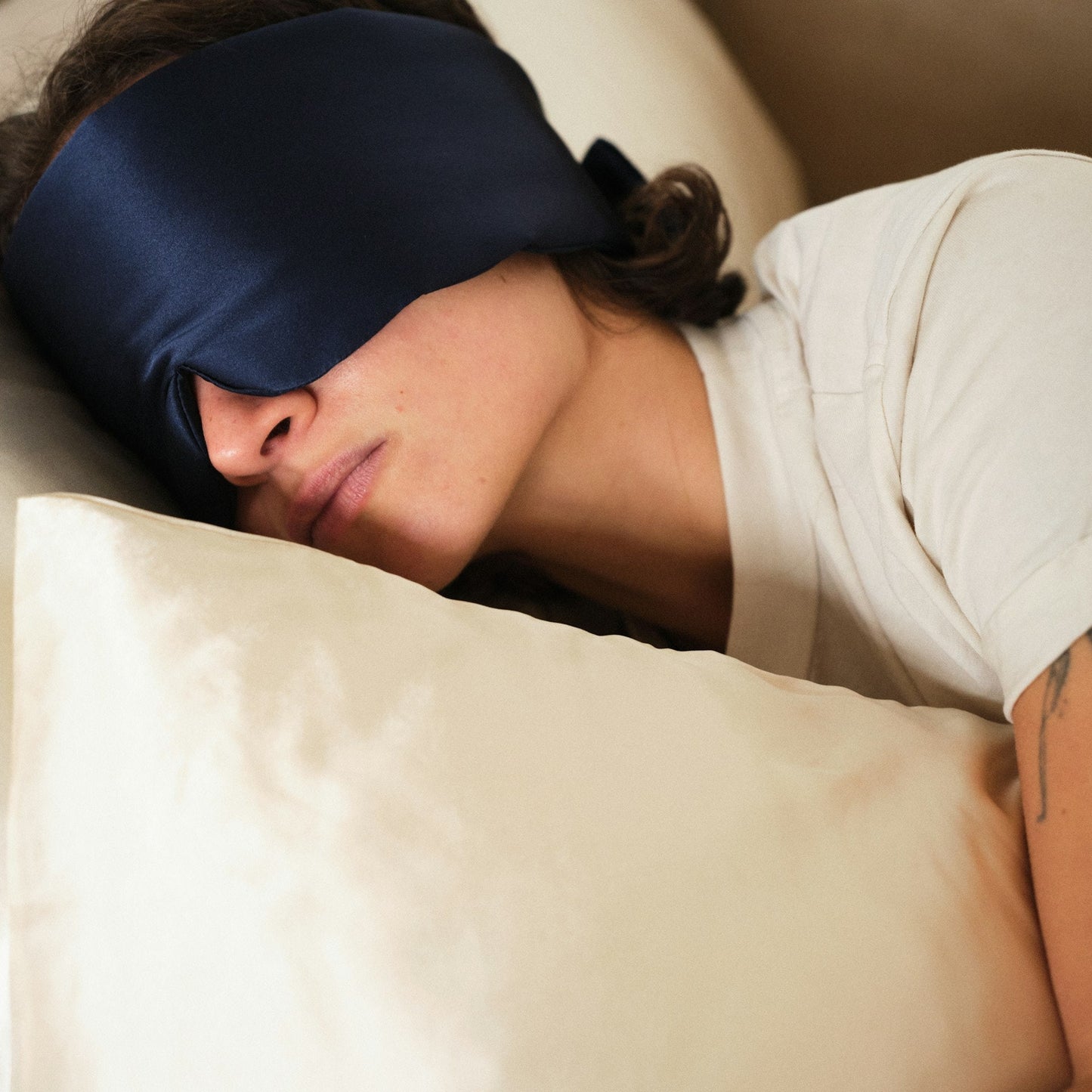 Person sleeping with a blue sleep mask on and a beige pillow. 